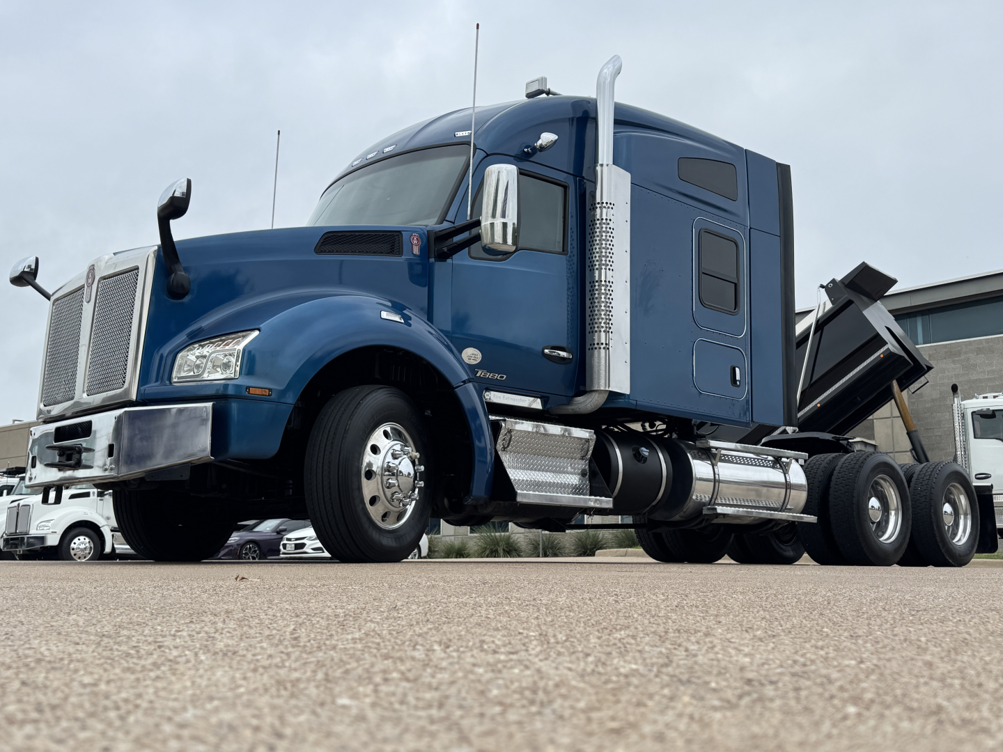 2019 Kenworth T880 conventional sleeper truck shown from a low-angle front-left view with blue cab, chrome fuel tanks, and dual rear axles.