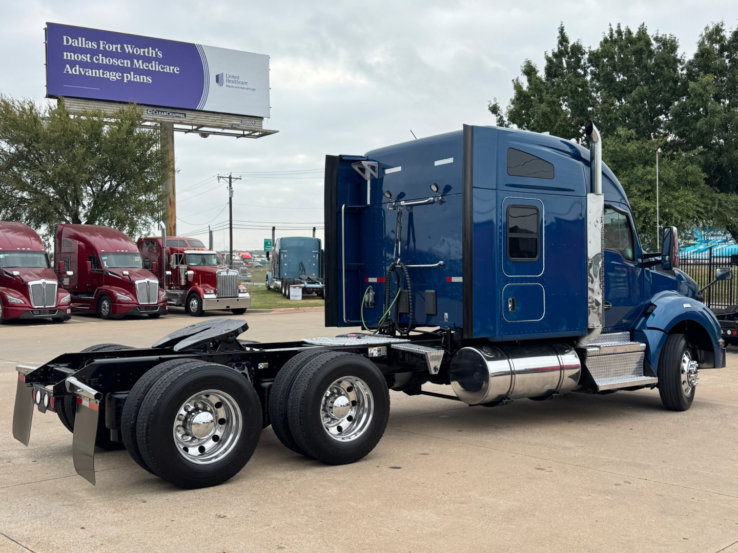 Kenworth T880 conventional sleeper truck, blue cab with rear chassis and dual rear axles, fuel tanks visible, set in a dealership lot.