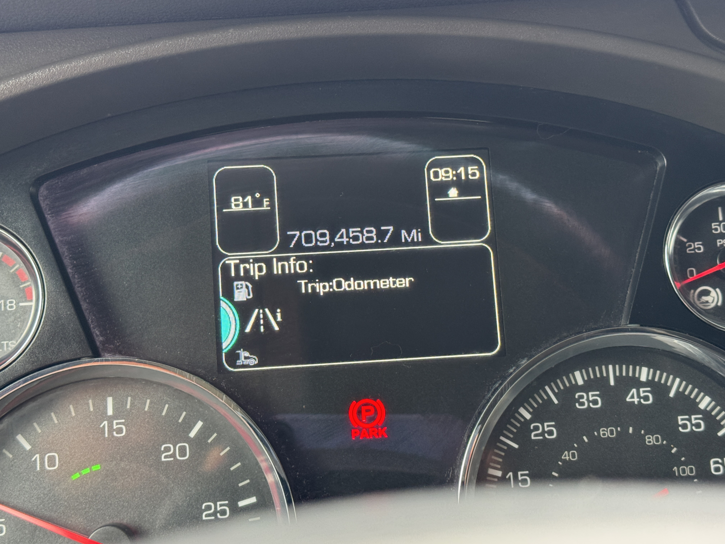Dashboard display of a Kenworth truck showing Trip Info: Trip Odometer, 81°F outside temp, 09:15, and odometer reading 709,458.7 mi. Gauges and Park brake indicator visible.