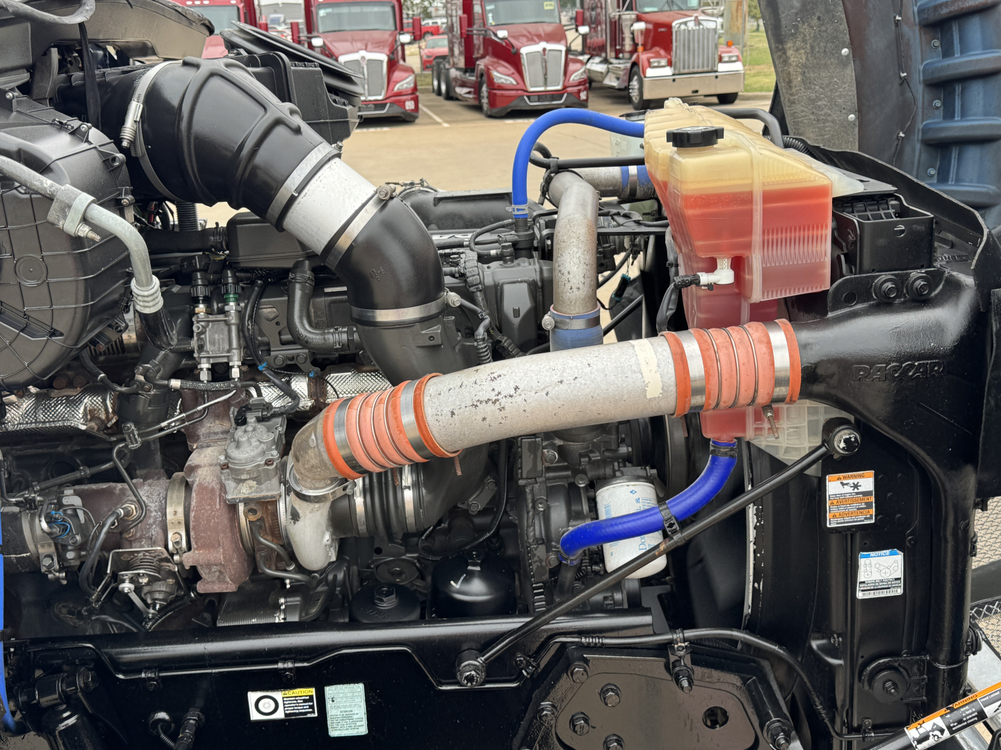 Kenworth T880 engine bay with intercooler piping, coolant reservoir, hoses, and turbo visible.