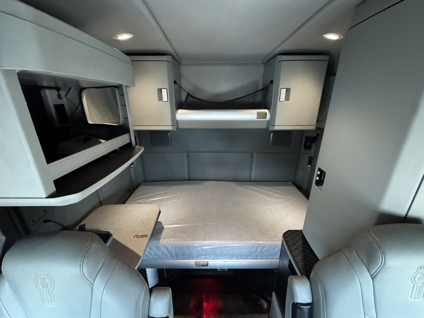 Kenworth T880 sleeper cab interior showing bunk bed with storage cabinets and overhead compartments.