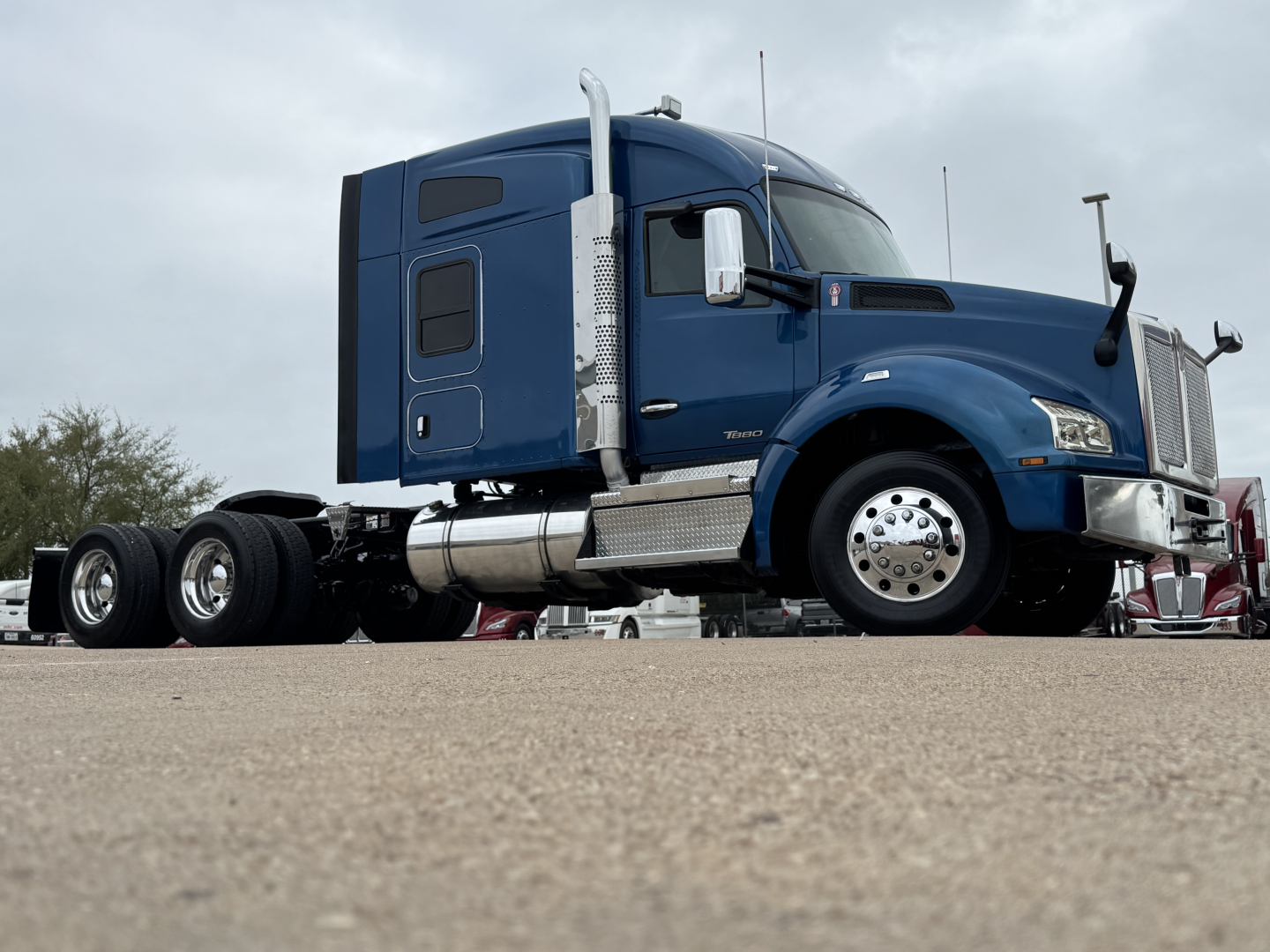 Kenworth T880 sleeper cab tractor in blue, side view showing fuel tanks, chrome wheel covers, and large front grille.