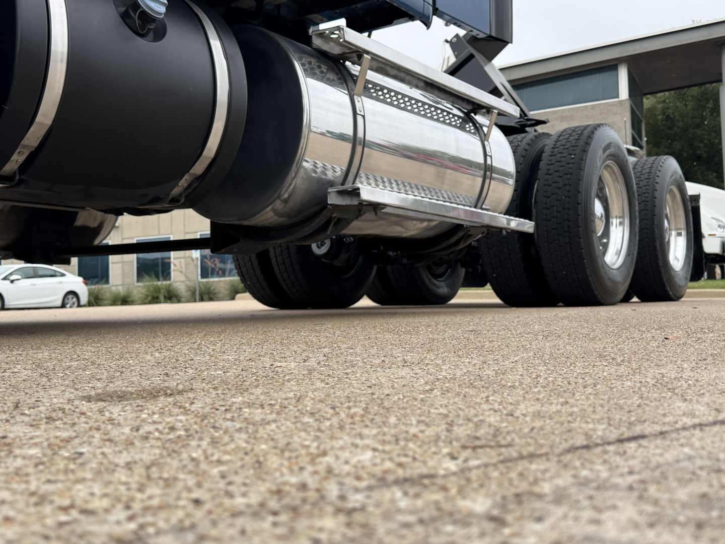 Kenworth T880 undercarriage showing chrome fuel tank and dual rear wheels from a low-angle view.