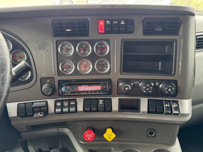 Kenworth T880 dashboard showing multiple round gauges, climate controls, hazard button, and storage compartments in a sleeper truck interior.