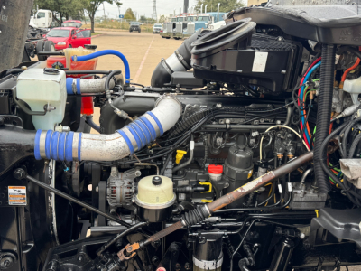 Kenworth T880 engine bay showing turbo intake and various hoses and wiring; blue silicone hoses, coolant reservoir, battery, and engine components visible.