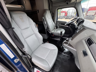Interior of a 2019 Kenworth T880 truck cab showing grey driver and passenger seats, steering wheel, dashboard, gear selector, and door view.