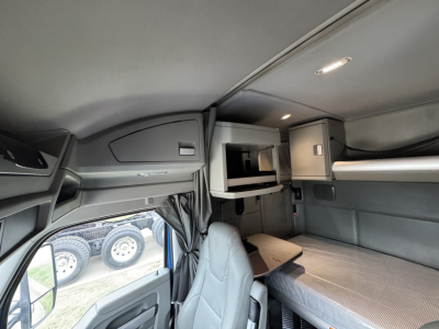 Cab interior of a 2019 Kenworth T880 sleeper truck showing overhead bunk, storage compartments, and seating area with table.