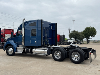 Kenworth T880 tractor viewed from side, blue sleeper cab with shiny polished fuel tanks and dual rear axles, no trailer attached.