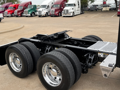 Kenworth T880 chassis show rear axle triple-axle configuration with dual rear wheels and metal deck plate; multiple tractors in background.