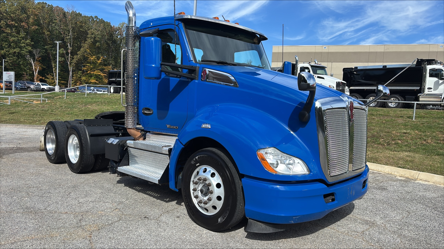 Kenworth T680 conventional daycab truck in blue, side view showing cab, chrome exhaust stack, and dual rear axles.