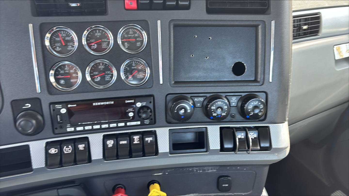 Kenworth truck dashboard with multiple gauges, radio, and climate controls; center console showing switches and knobs.