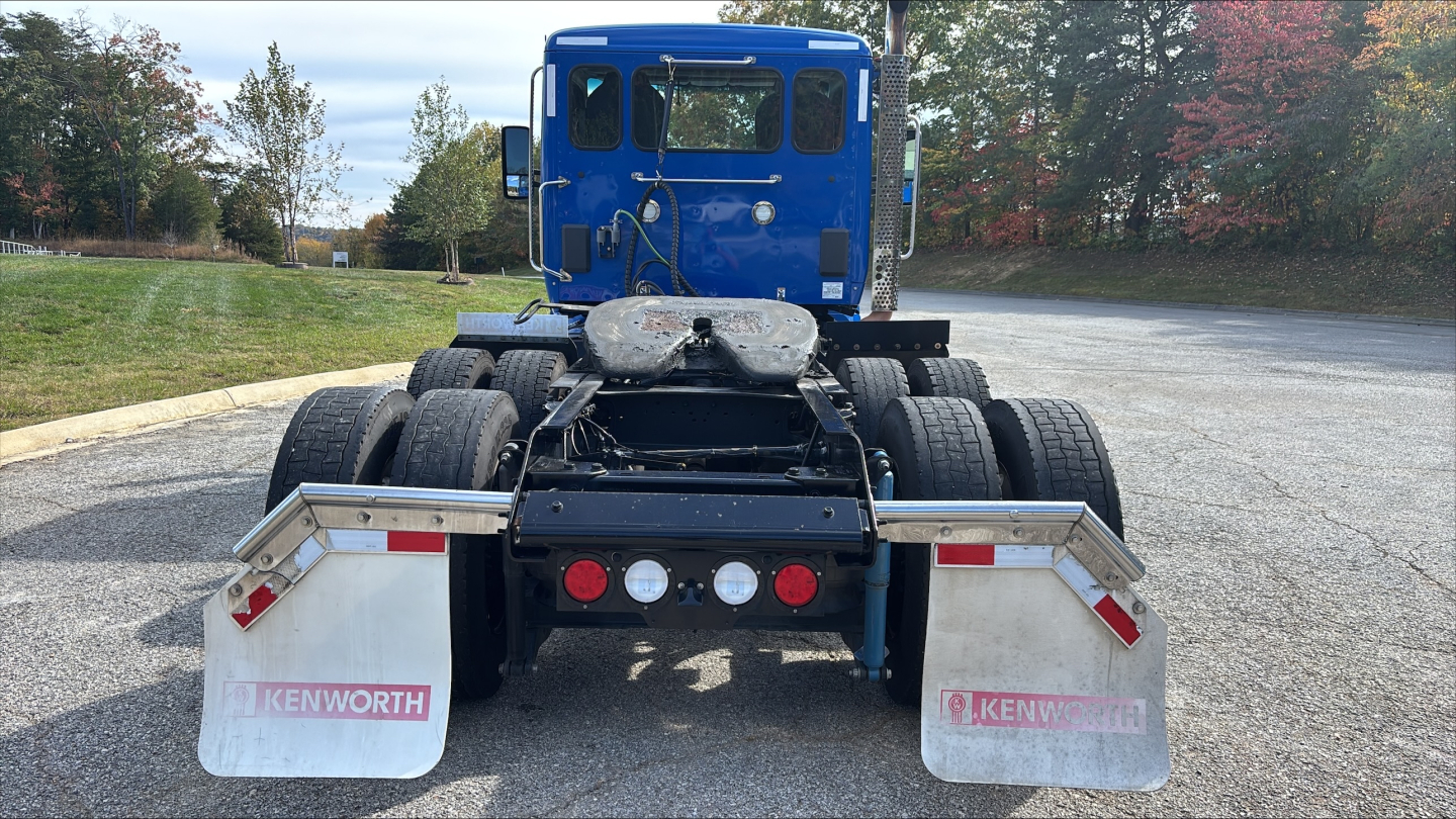 Rear view of a 2021 Kenworth T680 daycab tractor showing dual rear axles, fifth-wheel plate, and two Kenworth mud flaps with red reflectors.