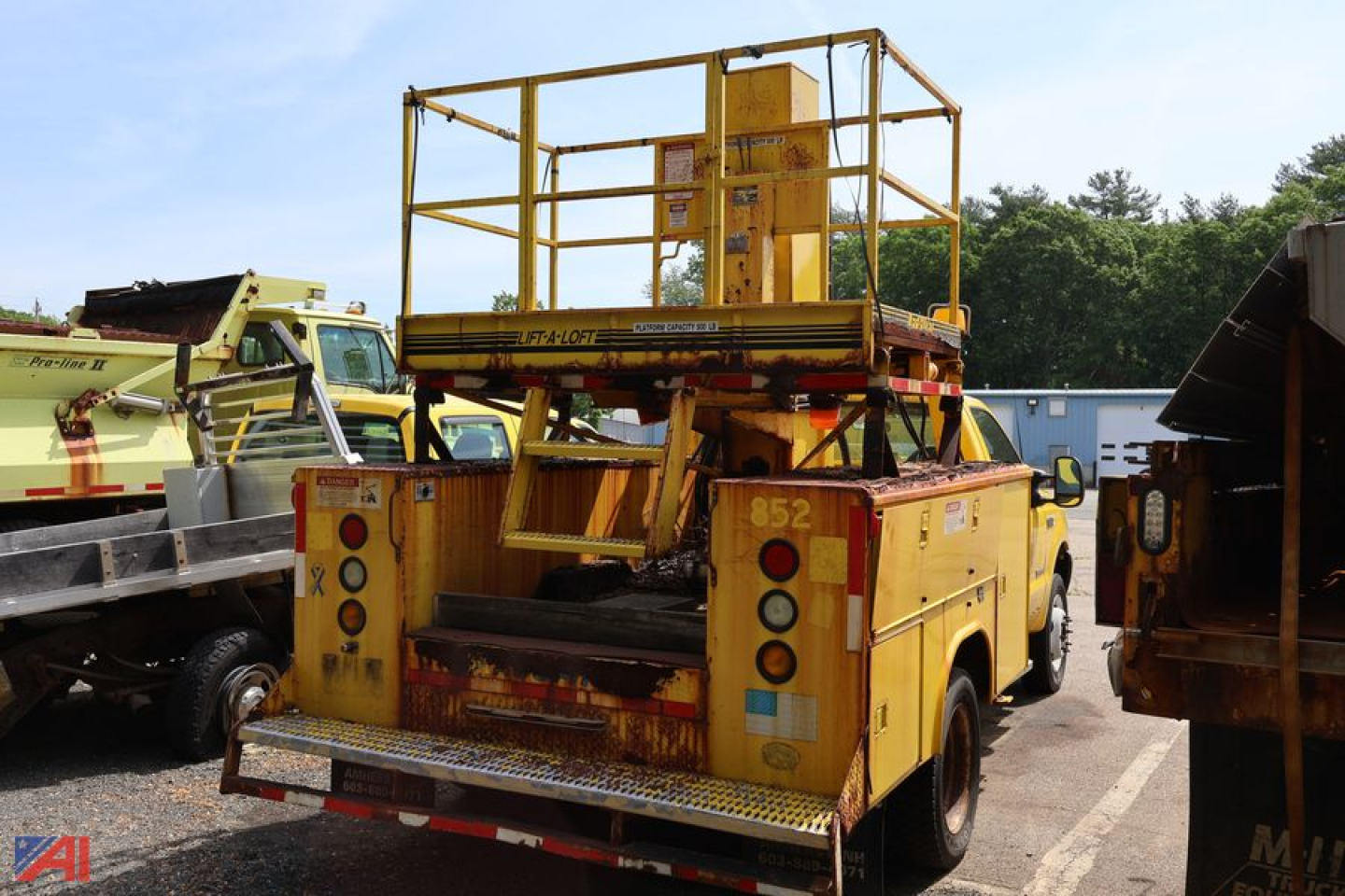 Rear view of a yellow utility lift truck in a used equipment lot with platform and railing, Ford F-550 chassis.