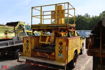 Rear view of a yellow utility lift truck in a used equipment lot with platform and railing, Ford F-550 chassis.