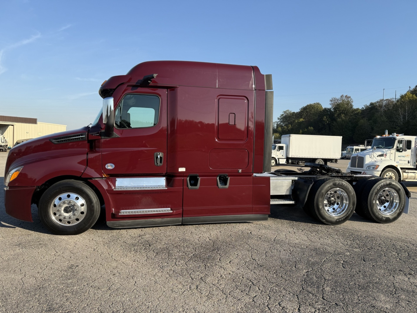 Image of a maroon Freightliner Cascadia 126 sleeper cab tractor, side view showing chrome exhaust and dual rear axles.