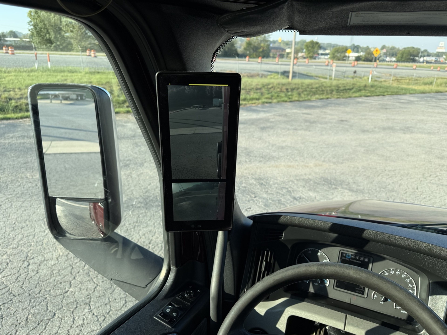 Truck cab interior of a 2021 Freightliner Cascadia126 showing the steering wheel, dashboard, large vertical dual-screen tablet mounted near the A-pillar, and side mirror.
