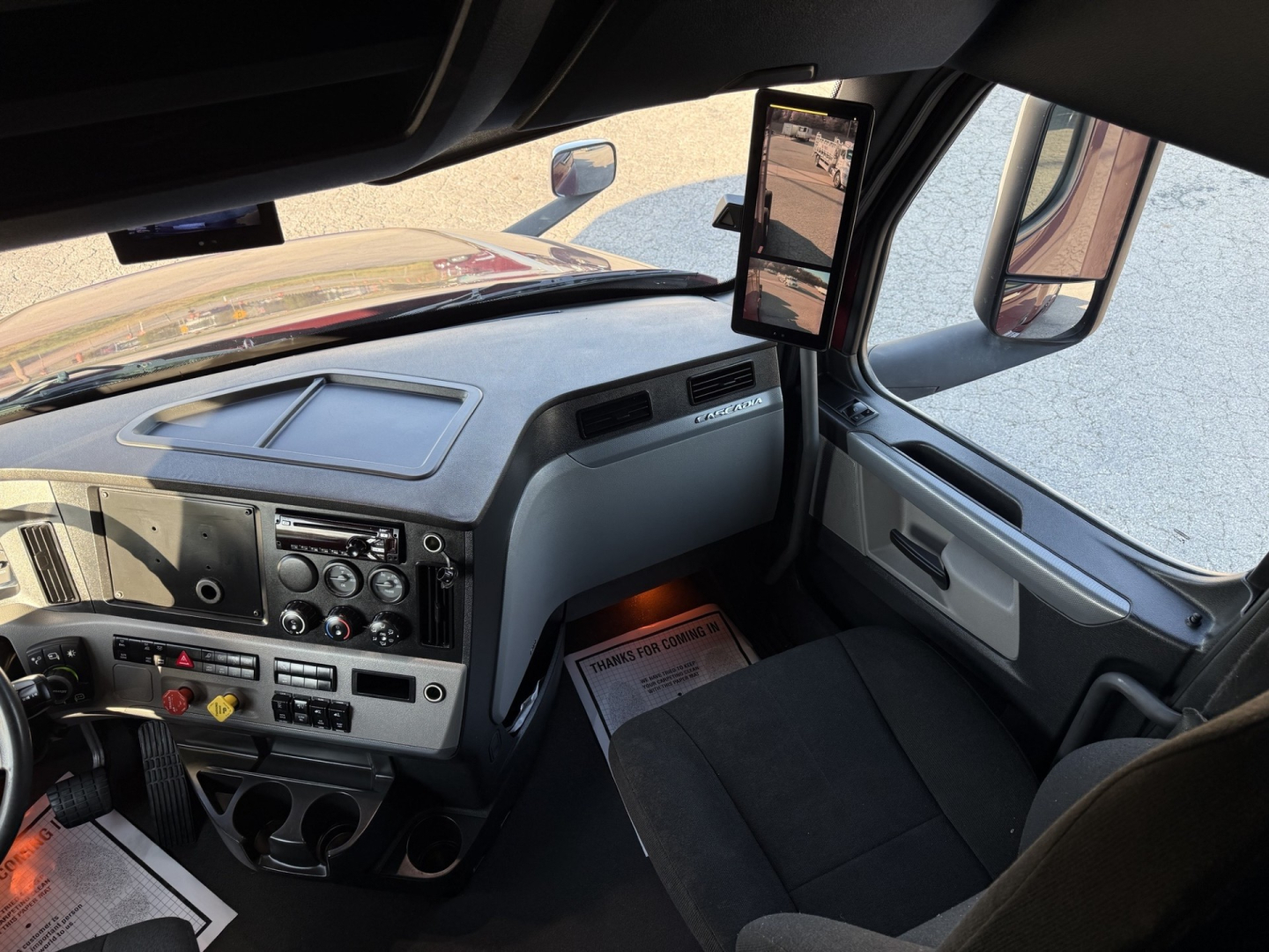 Cab interior of 2021 Freightliner Cascadia126 truck showing dashboard controls, steering column, center console with gauges and vents, side mirror and window.
