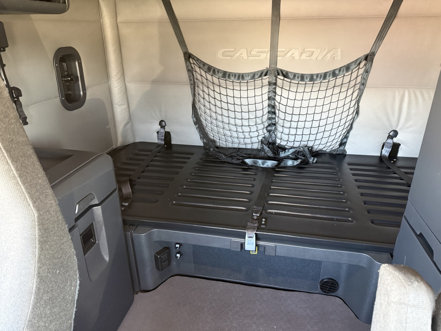 Freightliner Cascadia126 sleeper cab interior cargo area with netting and strap in view, showing bed platform and storage compartments.