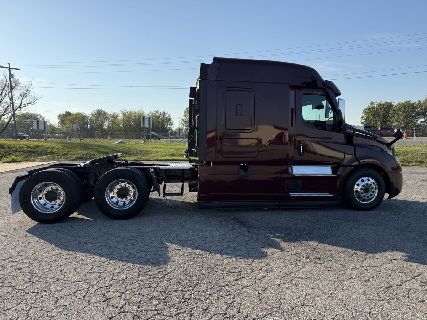 Freightliner Cascadia126 tractor shown in side profile with two rear axles, dark maroon paint, cab and chassis visible.