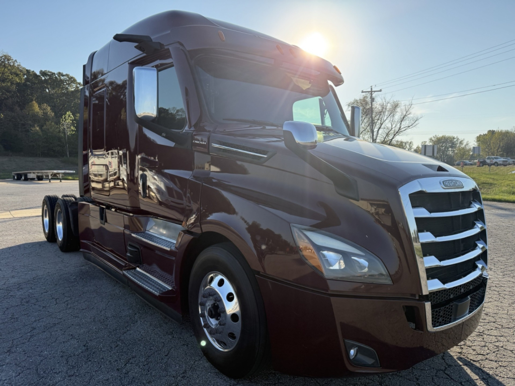 Freightliner Cascadia 126 tractor-trailer in dark brown, front three-quarter view, chrome grille, sleeper cab, daylight.