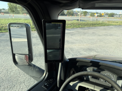Truck cab interior of a 2021 Freightliner Cascadia126 showing the steering wheel, dashboard, large vertical dual-screen tablet mounted near the A-pillar, and side mirror.