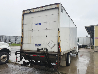 Rear view of a white Kenworth T-300 box truck trailer with rusty edges and a black landing gear, showing closed rear doors and a small blue sticker.