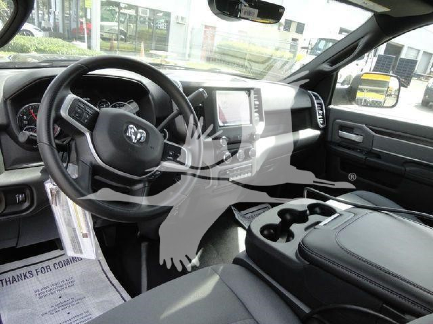 Ram pickup truck interior showing steering wheel with Ram badge, center touchscreen display, gear selector, and cupholders in the console.