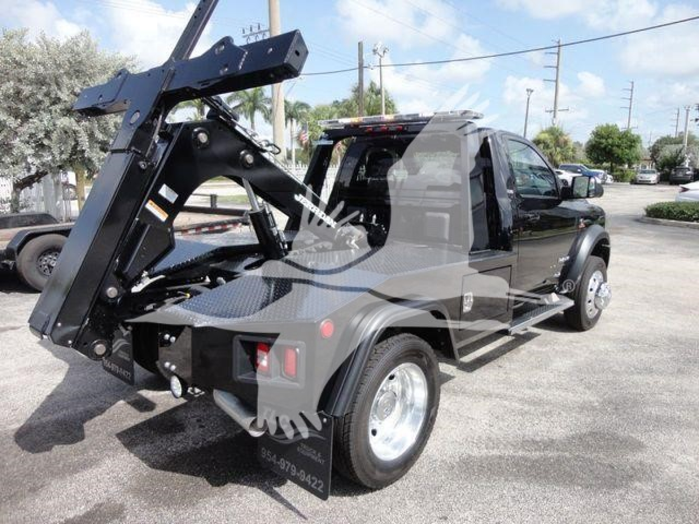 Truck bed with heavy-duty hydraulic winch attachment mounted on a Ram 4500 SLT pickup; rear side shows wheel, tail light, and bumper; clear sky and dealership lot in background.