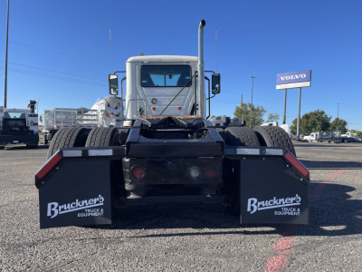 Rear view of a 2020 Mack AN64T daycab truck chassis showing dual rear wheels, mud flaps with Brackner's Truck & Equipment logo, exhaust stack, and a Volvo sign in the distance.