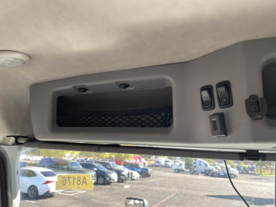 Cab interior overhead with storage pocket and switches in a 2020 Mack AN64T daycab, showing overhead console and window view. Specific text not legible.
