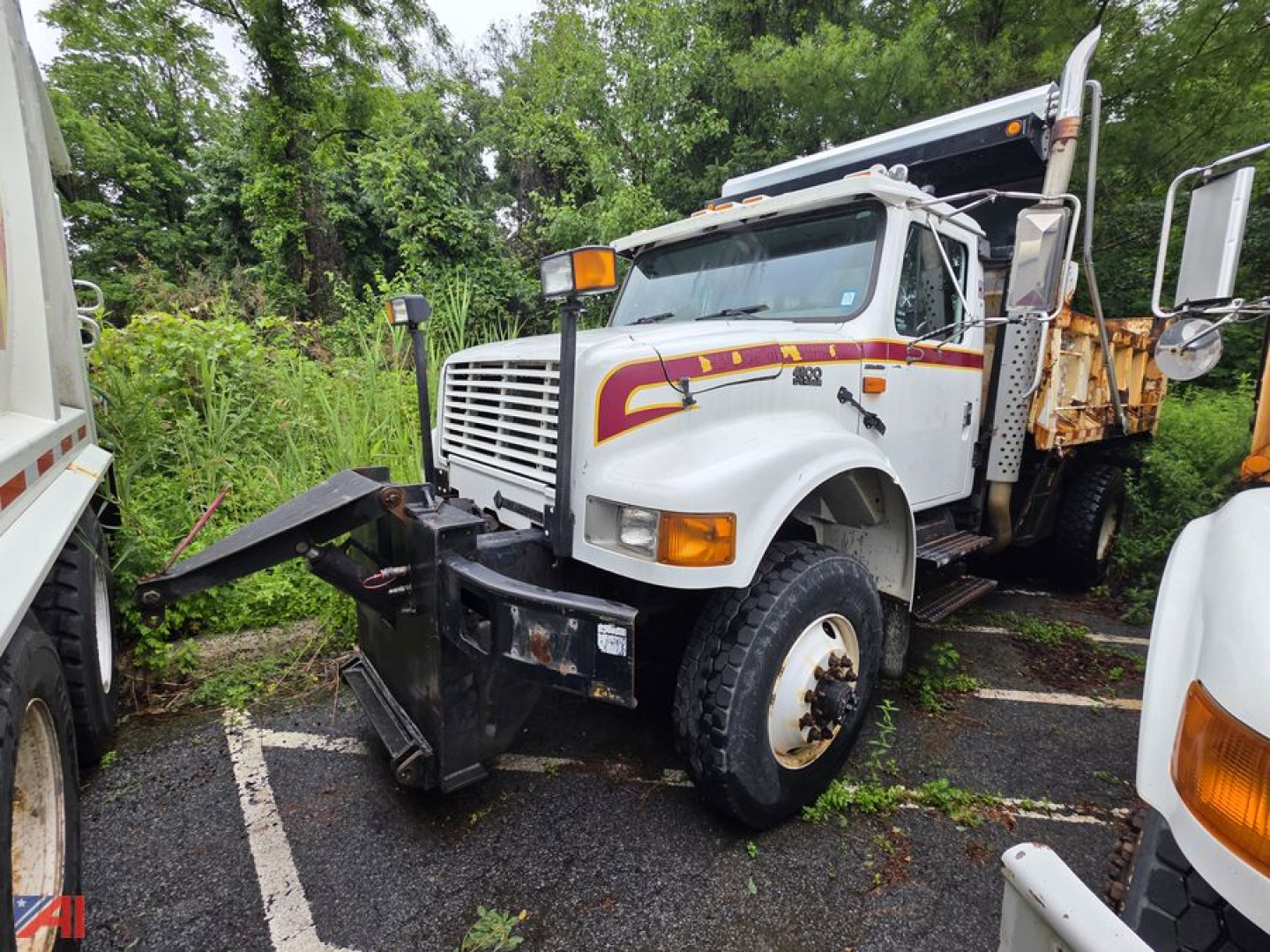 Dump truck with front plow attachment, white cab, International logo, and yellow rear bed in a salvage lot.