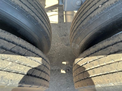 Trailer wheels in close-up showing dual rear tires with tread and gravel on ground between them, part of a dump trailer with electric tarp system.