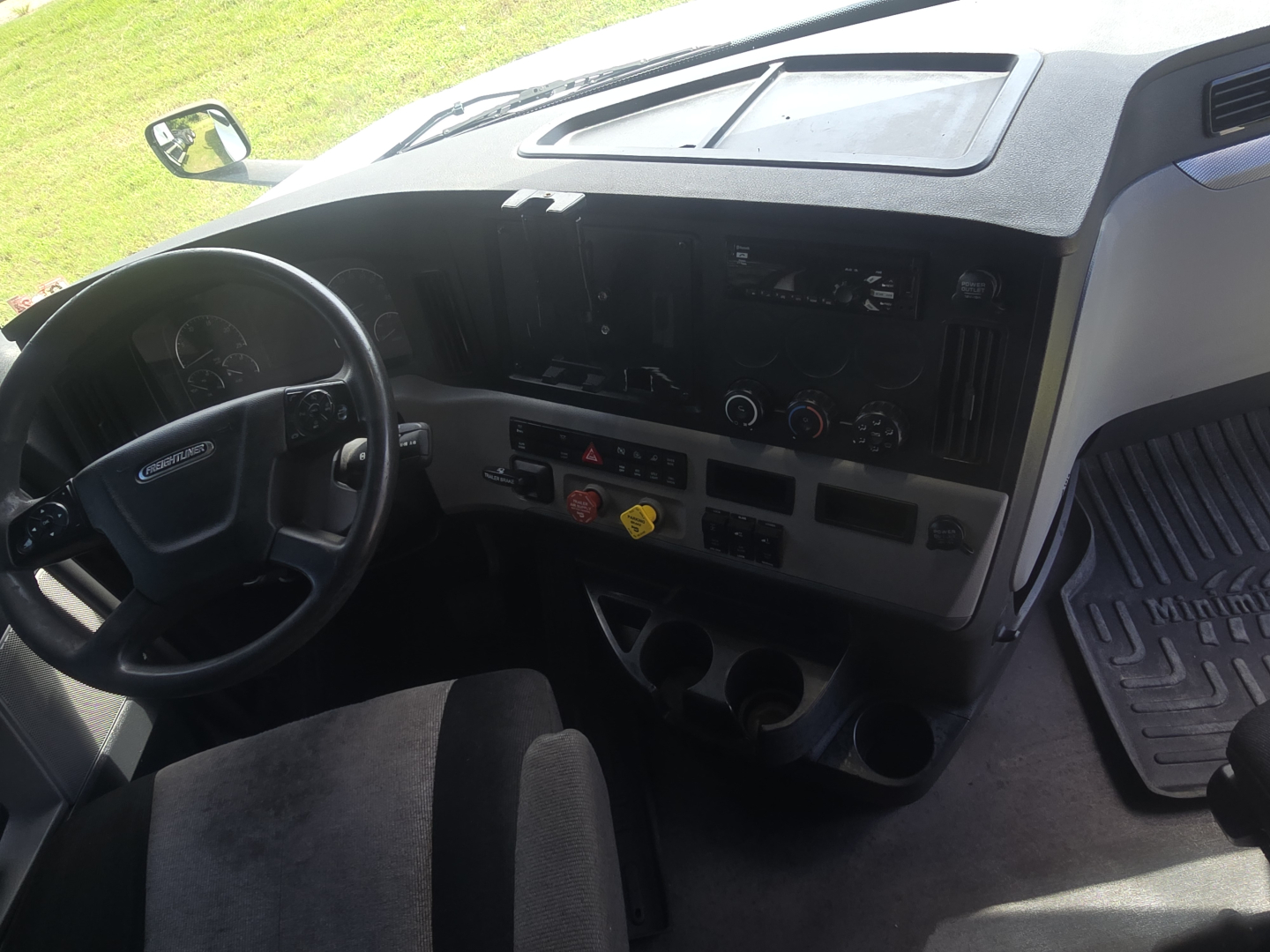 Dashboard and steering wheel of a Freightliner Cascadia truck cab interior with center console controls and cup holders.