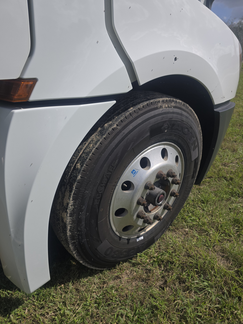 Truck front wheel showing rim and tire on the left side of a white Freightliner Cascadia cab.