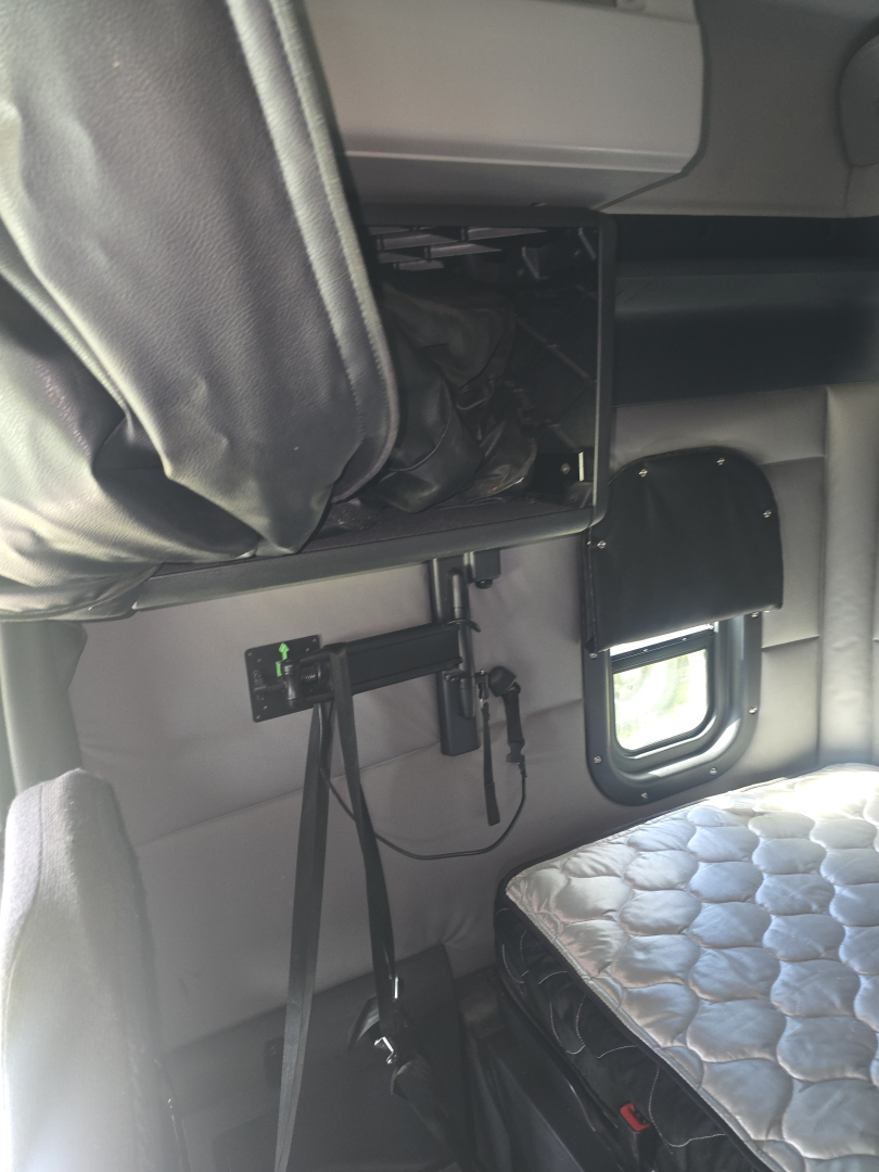 Truck interior showing bunk area and equipment panel with tablet holder and control switches in a Freightliner Cascadia sleeper cab.