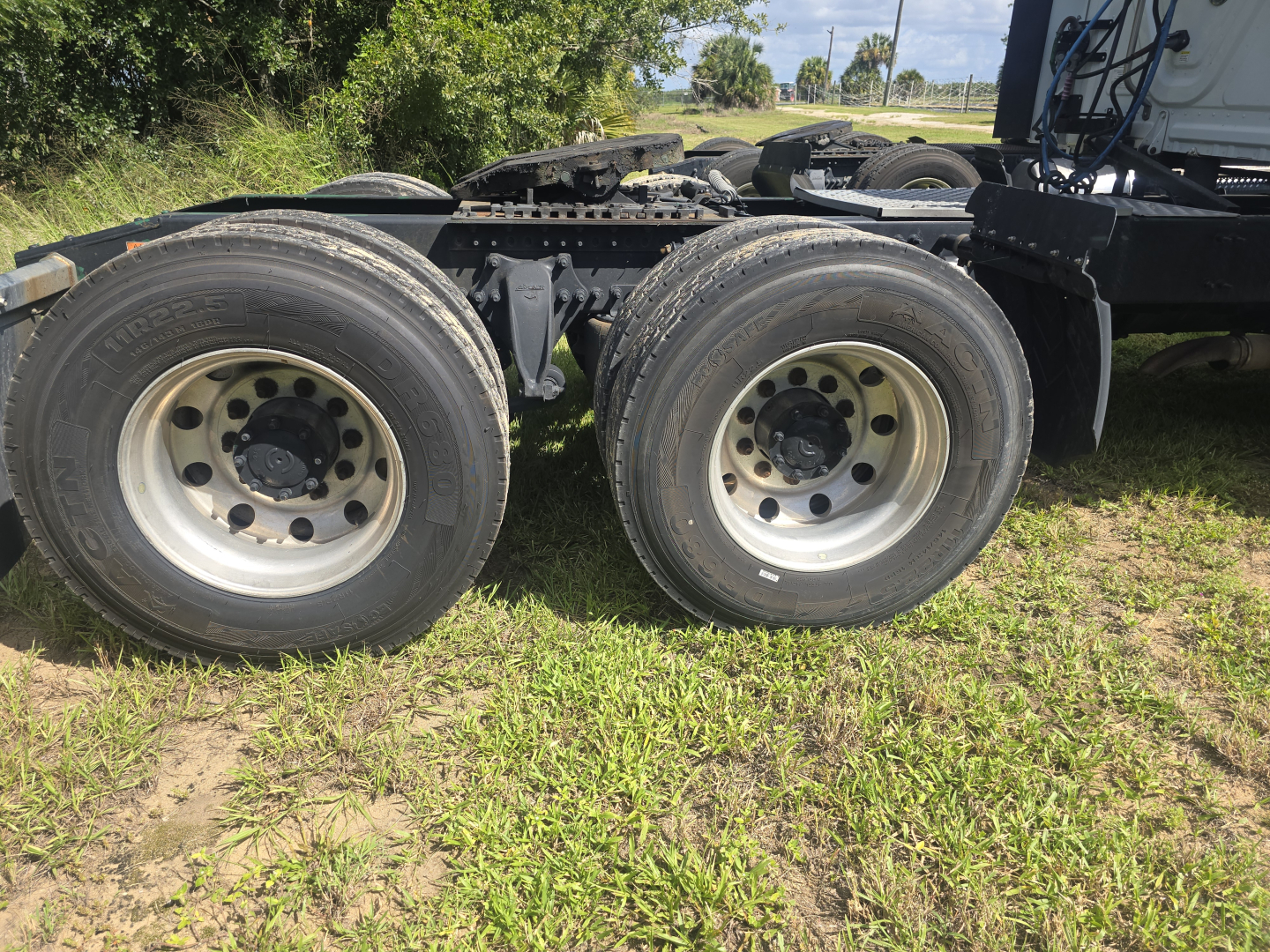 Tractor-trailer dual rear axles showing tires and rims on a Freightliner Cascadia tractor frame, with suspension and fifth-wheel area visible.
