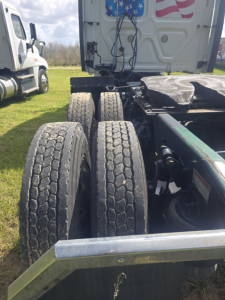 Truck chassis showing dual rear axles and rear suspension under a Freightliner Cascadia tractor, with tires and frame visible.