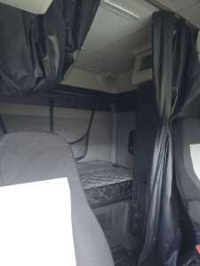 Truck cab interior showing bunk area with mattress, partition curtains, and overhead storage from a Freightliner Cascadia sleeper cab.