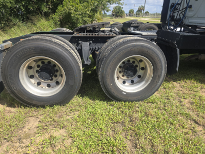 Tractor-trailer dual rear axles showing tires and rims on a Freightliner Cascadia tractor frame, with suspension and fifth-wheel area visible.
