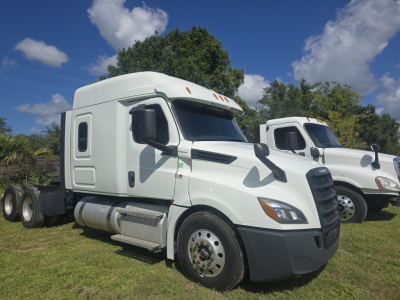 Truck tractor with white cab showing side view, front grille, fuel tanks, and two rear axles in a grassy lot