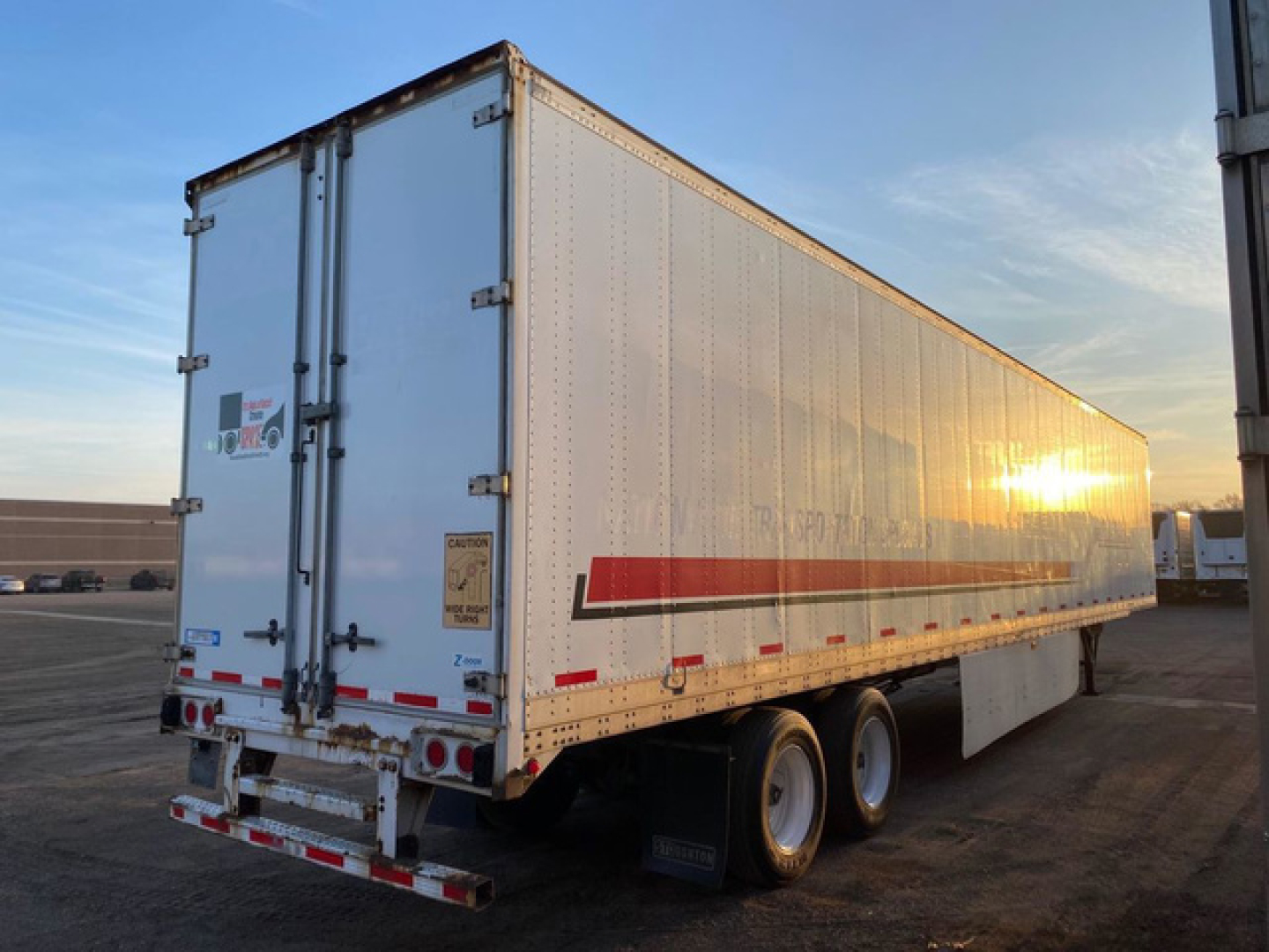 Trailer side and rear showing 2013 Stoughton van trailer with twin rear doors and red reflective stripe, sunset glare on aluminum body, dual rear tires.