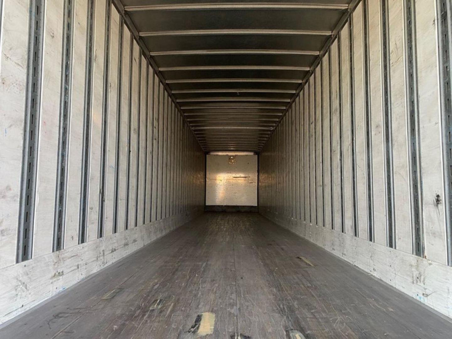 Trailer interior showing long metal box with side rails and wooden floor, empty with light at far end.