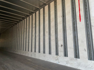 Trailer interior showing metal wall ribs and wooden floor with ridges; light at far end.