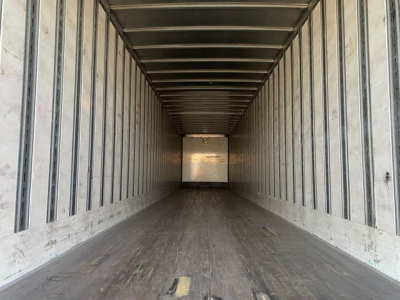 Trailer interior showing long metal box with side rails and wooden floor, empty with light at far end.