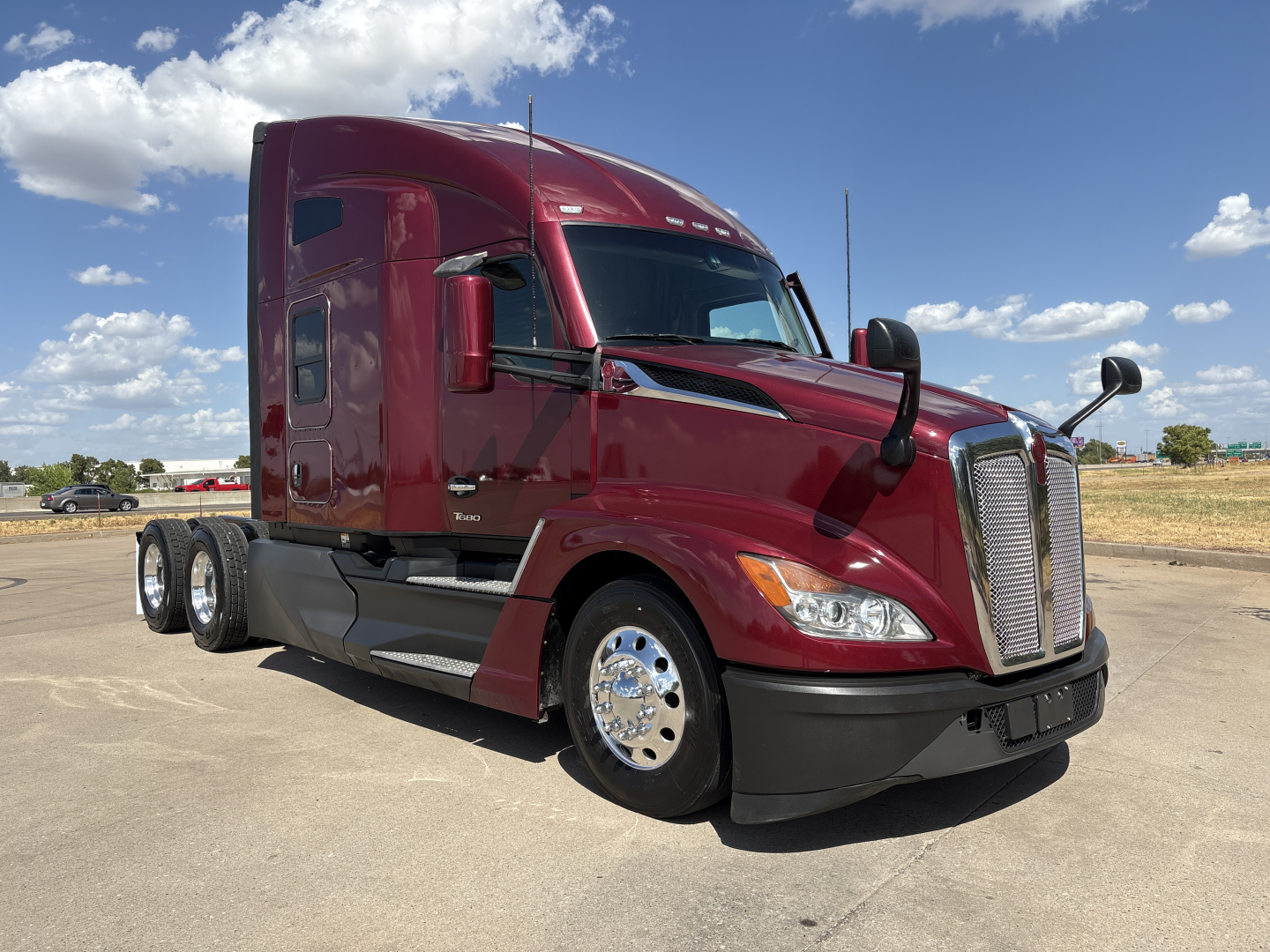 Kenworth T680 day cab tractor in maroon with chrome wheels, side view showing sleeper cab, front grille, and dual rear axles.