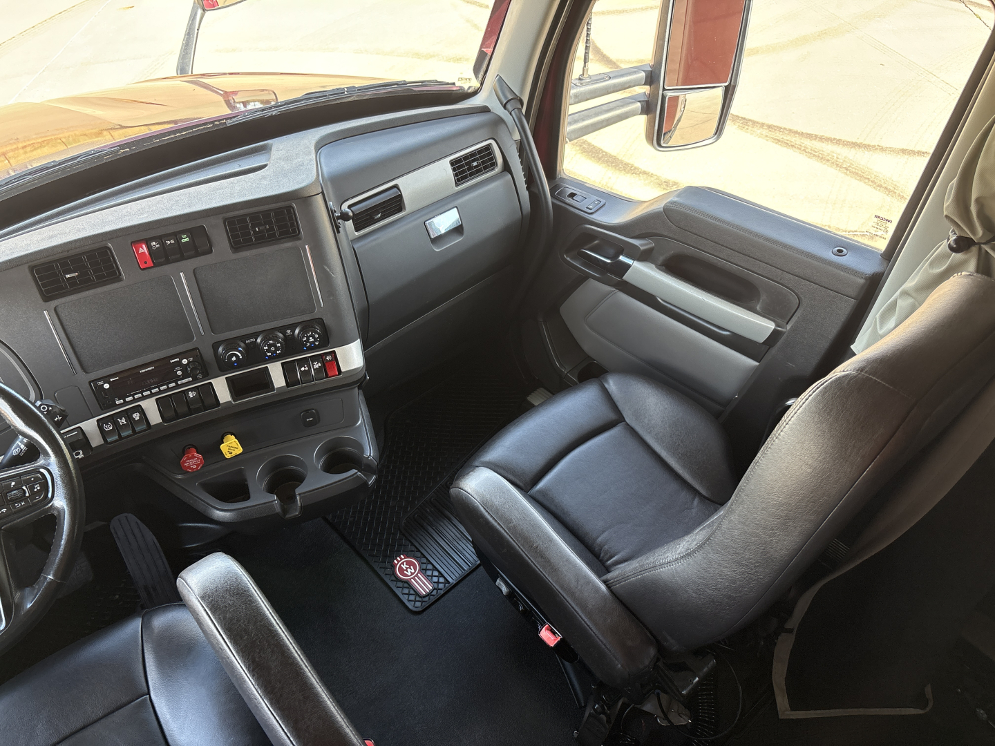 Cab interior of a 2023 Kenworth T680 truck showing driver seat, dashboard, and steering wheel with control panels and gear shifter.