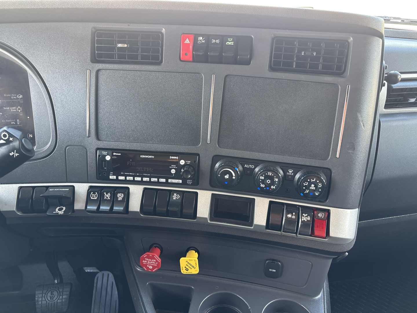 Kenworth T680 dashboard and center console showing four blank screens, controls, and a red hazard switch with climate and radio panel.