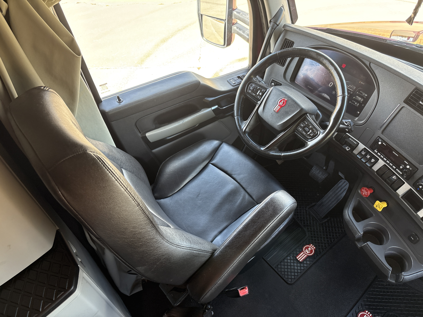 Kenworth T680 driver’s area with steering wheel, dashboard, and black leather seat visible.
