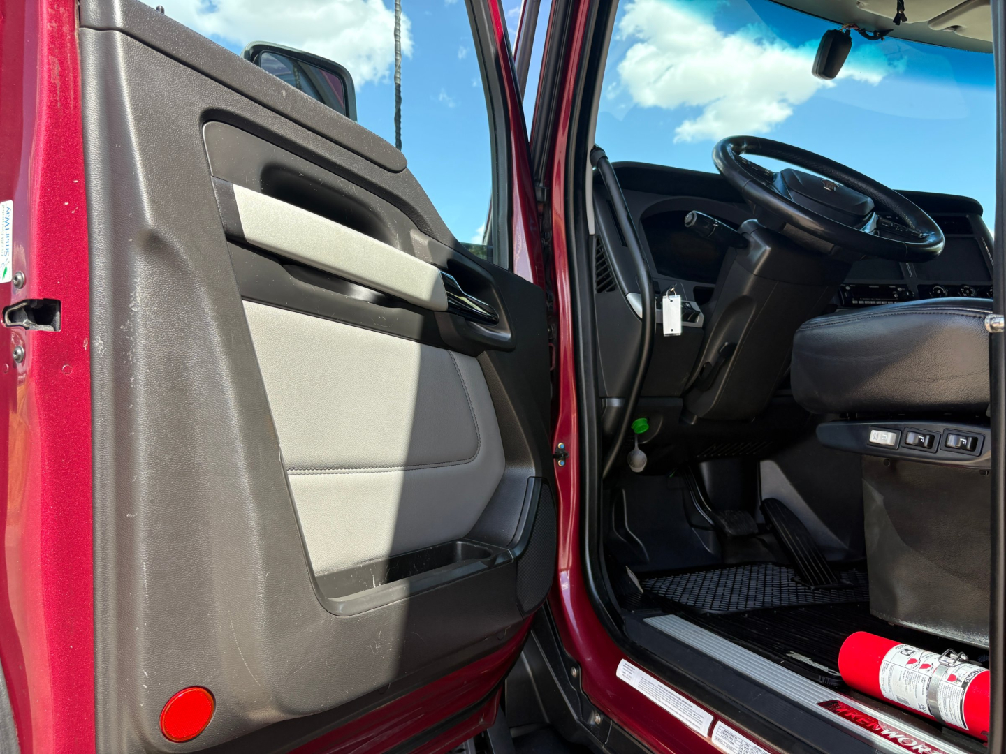 Truck cab interior of a 2023 Kenworth T680 featuring open driver’s door, steering wheel, and dashboard visible.