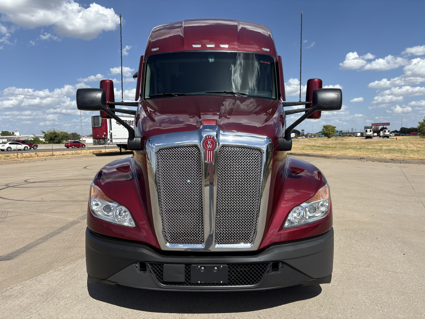 Kenworth T680 front view showing chrome grille, headlights, and emblem, red in color, in a parking lot.